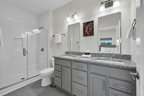 A modern bathroom with a walk-in shower, a toilet, a vanity with a granite countertop, and a large mirror. - Superb Southside Townhome (Asheville)