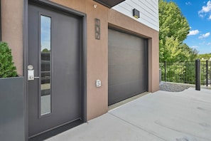Un bâtiment moderne doté d’une porte de garage et d’une grande porte d’entrée de couleur sombre.