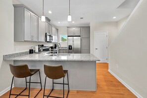 A modern kitchen with granite countertops, stainless steel appliances, and bar stools.