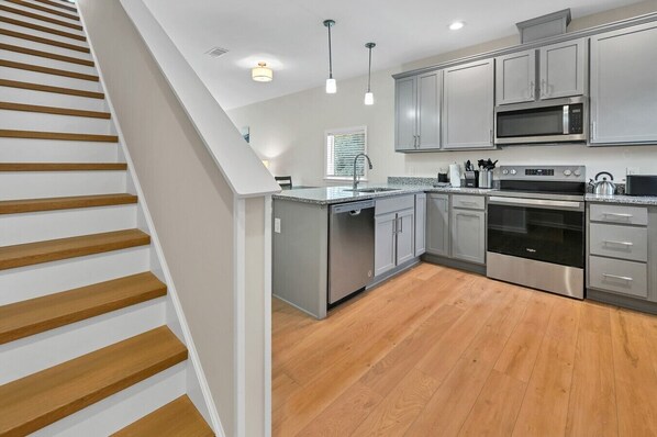A modern kitchen with grey cabinets, stainless steel appliances, and a wooden staircase.