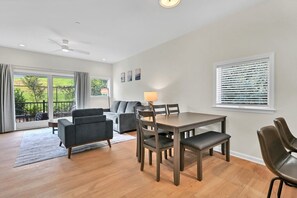A modern living room with a dining area, large windows, and a view of the outdoors.
