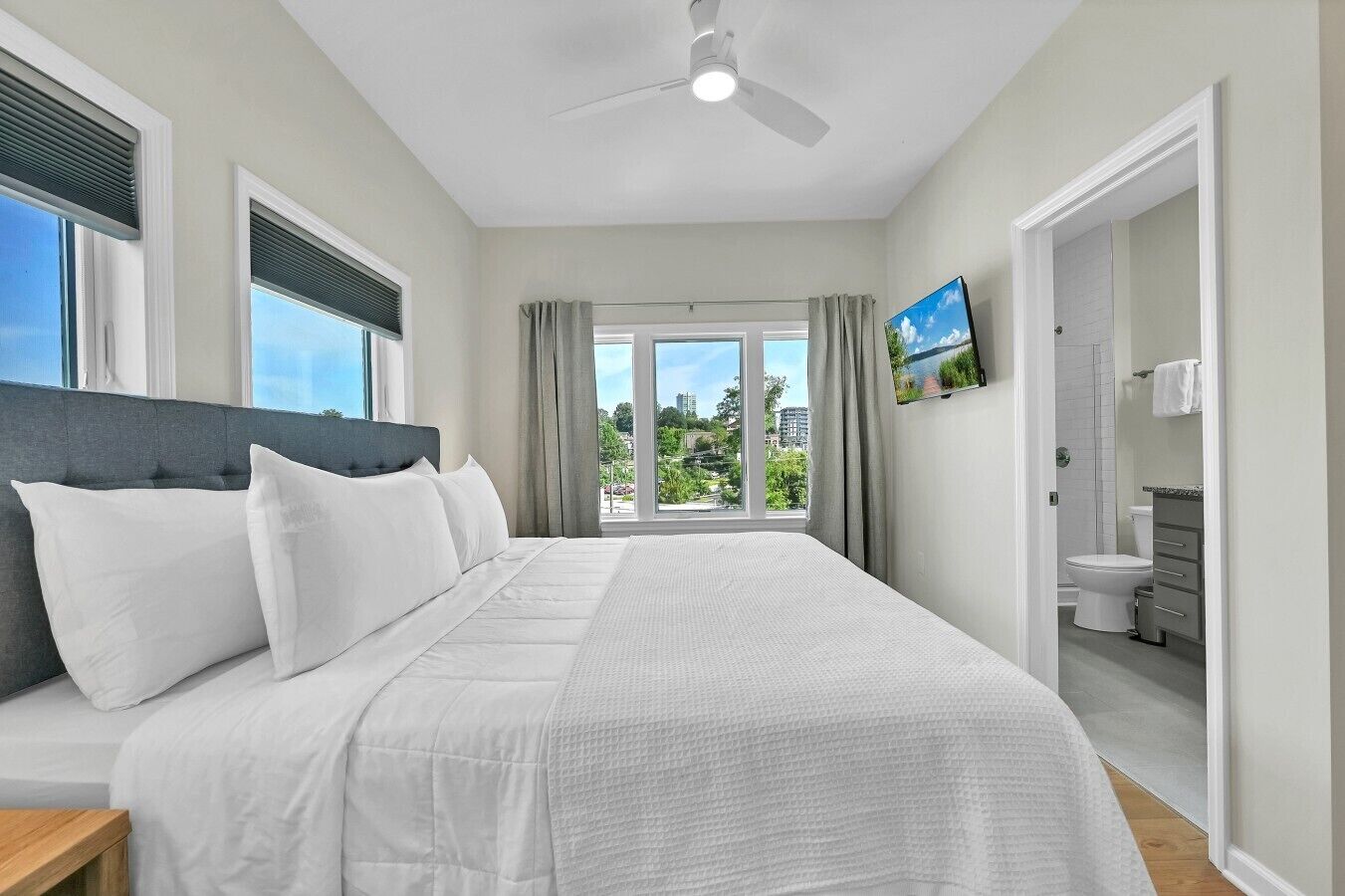 Une chambre à coucher avec un lit, un ventilateur de plafond, un téléviseur et une vue sur l’extérieur.