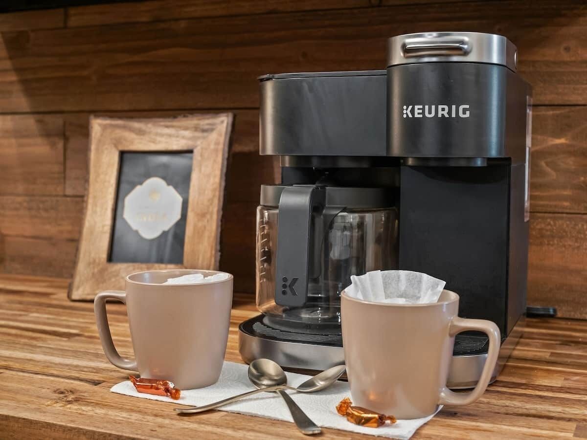 A Keurig coffee maker with two cups of coffee and a spoon on a wooden table.