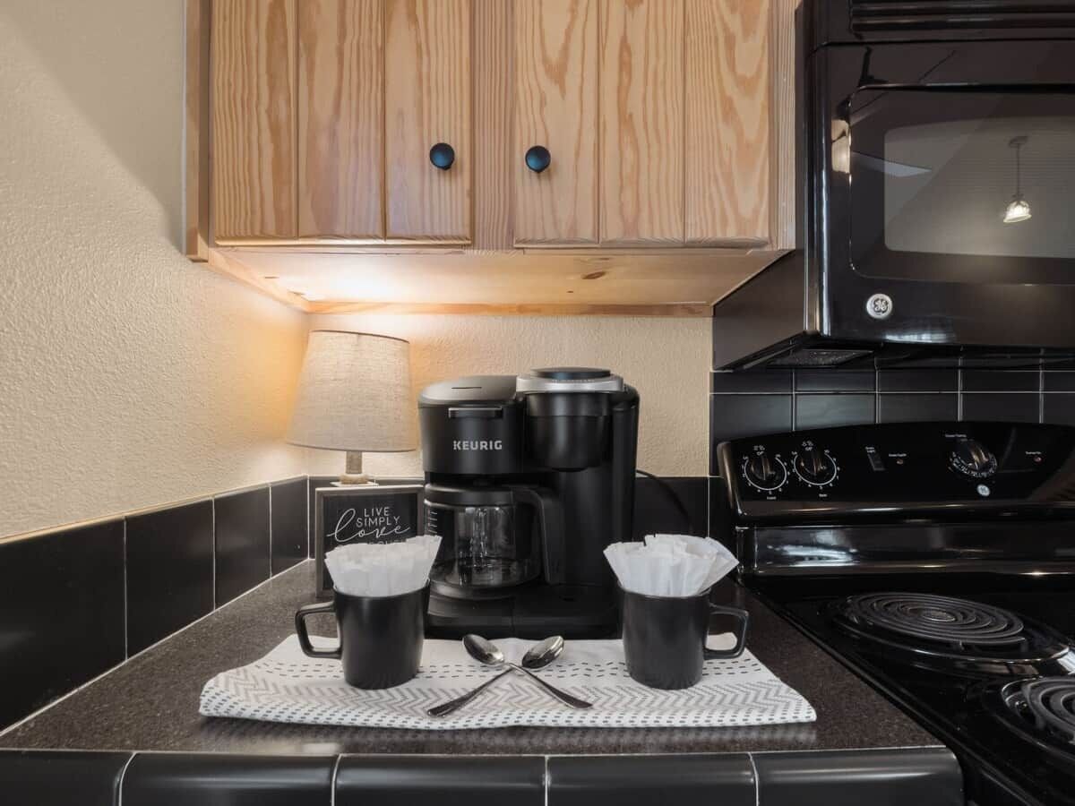 Een keuken met een koffiezetapparaat, twee mokken, een fornuis en een magnetron.