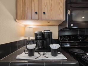 A kitchen with a coffee maker, two mugs, a stove, and a microwave.