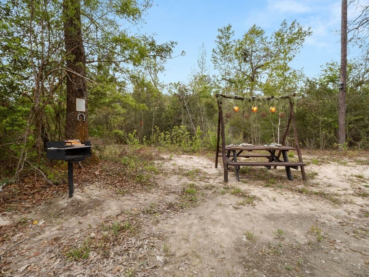 Une table de pique-nique avec un banc et un panier suspendu, le tout situé dans une zone boisée.