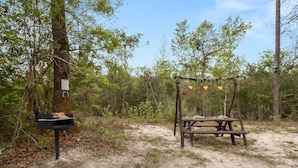 A picnic table with a bench and a hanging basket in a wooded area.