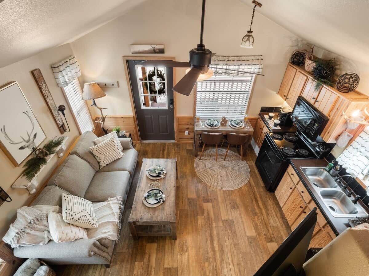 Un espace de vie compact comprenant un canapé, une table basse, une table à manger, un coin cuisine et un ventilateur de plafond.