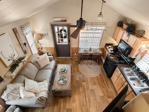 A compact living space with a sofa, coffee table, dining table, kitchen area, and a ceiling fan.
