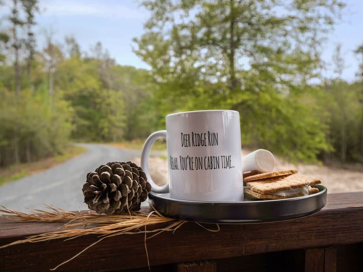 Une tasse ornée d’un message, une pomme de pin et une assiette avec un biscuit, le tout posé sur une surface en bois.