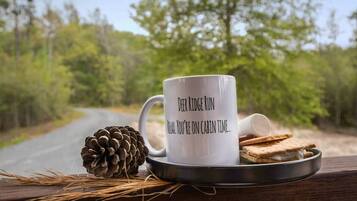Une tasse ornée d’un message, une pomme de pin et une assiette avec un biscuit, le tout posé sur une surface en bois.