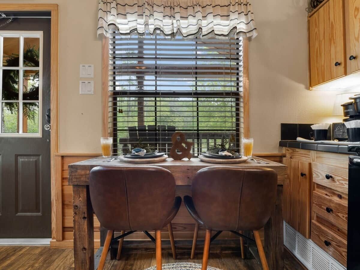 Un coin repas avec une table dressée pour deux personnes, une fenêtre avec des stores et des meubles en bois.