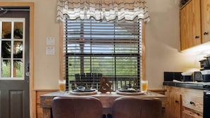 A dining area with a table set for two, a window with blinds, and wooden cabinetry.
