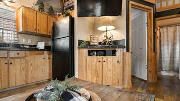 A kitchen with wooden cabinets, a black refrigerator, a dining table with a decorative centerpiece, and a wall-mounted television.