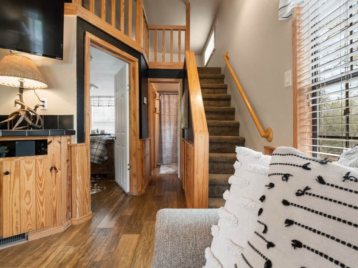 Eine Treppe führt zu einer zweiten Etage, mit Holzdielenboden, einem Fernseher und einem Fenster mit Jalousien.