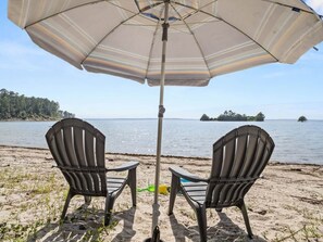 Zwei Adirondack-Stühle mit Blick auf einen See, ein Sonnenschirm spendet Schatten.