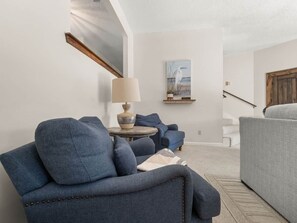 Ein Zimmer mit einem blauen Sofa, einem grauen Sofa, einem runden Tisch mit einer Lampe und einem Bild an der Wand.
