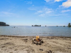 A beach with a fire pit in the foreground and a calm lake in the background. - Lakefront Beach Retreat w/ Kayaks & Fire Pit! (Sabine Parish)