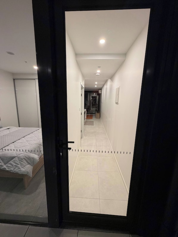 A hotel room with a bed, a door, and a hallway leading to a bathroom. - Brand new G6 Apartment (Canberra)