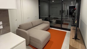 Una sala moderna con un sofá modular, un armario blanco y un ventanal que da a un balcón.