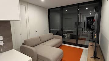 A modern living room with a sectional sofa, a white cabinet, and a glass door leading to a balcony.