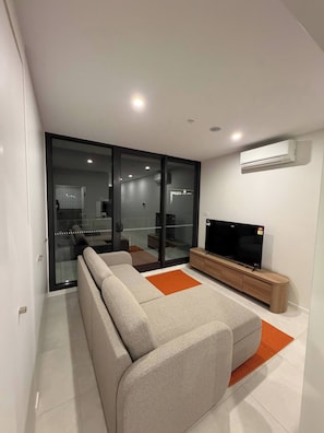 A modern living room with a sofa, a flat-screen TV, and an air conditioning unit. - Brand new G6 Apartment (Canberra)