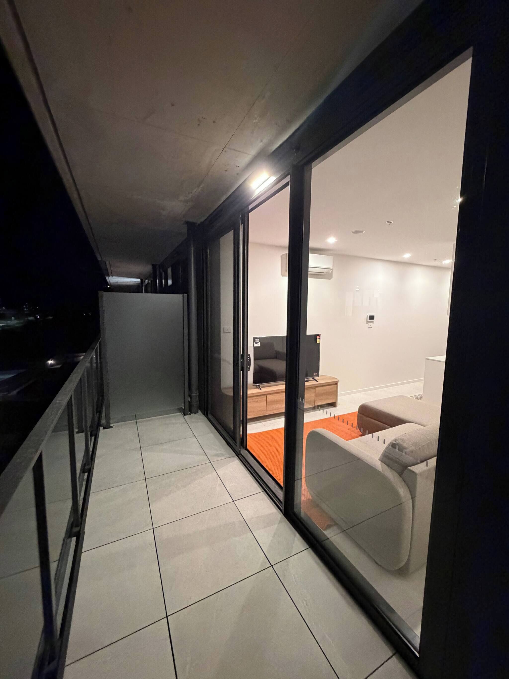 A corridor with a sliding glass door leading to a modern living area with a sofa and a coffee table.