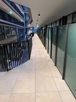 A corridor with glass partitions, a tiled floor, and a railing on one side. - Brand new G6 Apartment (Canberra)