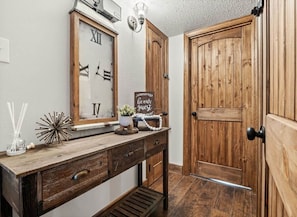 A wooden door with a black handle, a wooden-framed mirror with Roman numerals, and a small sign on the wall.