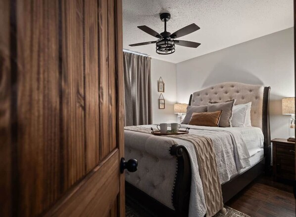 A bedroom with a bed, a ceiling fan, a nightstand, and a lamp.