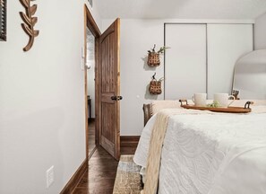 A bedroom with a bed, a wooden door, a wardrobe, and two wall-mounted baskets with plants.