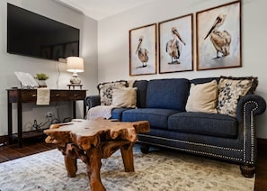 A living room with a blue sofa, wooden coffee table, and wall-mounted paintings of pelicans.