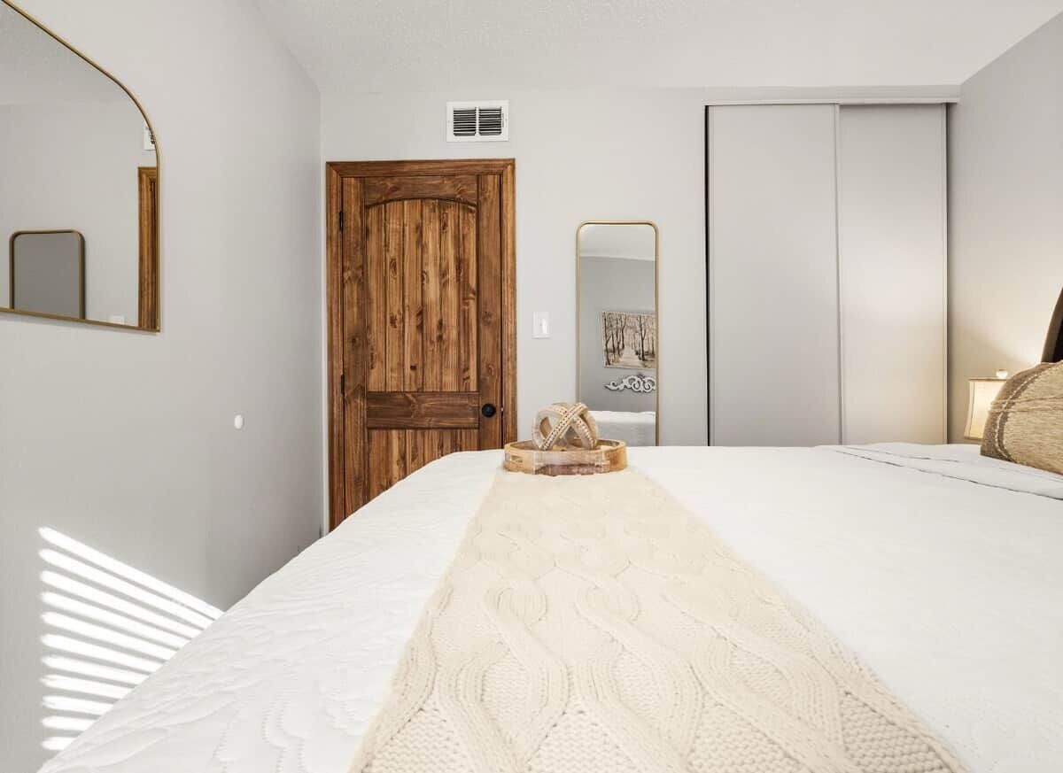 Un dormitorio con una cama, una puerta de madera, un espejo y un armario.