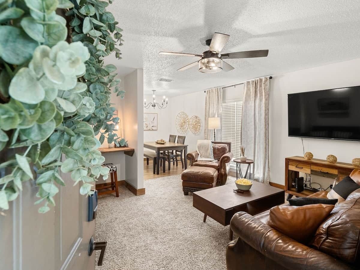 A living room with a brown leather sofa, a coffee table, a TV, and a ceiling fan.