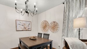 A dining area with a wooden table, chairs, a chandelier, and wall decor. - Fort Polk Cozy 2BR Stay l Monthly & Extended Stays (Leesville)