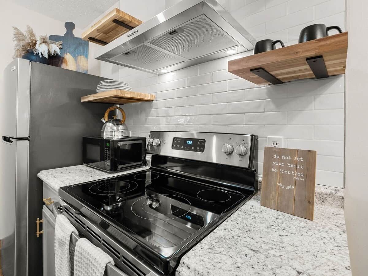 A kitchen with a stainless steel stove, microwave, and a wooden shelf above.