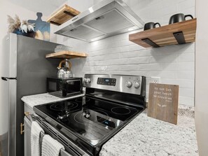 A kitchen with a stainless steel stove, microwave, and a wooden shelf above.