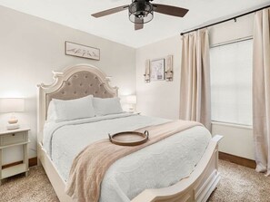 A bedroom with a bed, bedside lamps, a ceiling fan, and a window with curtains.