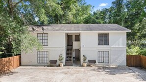 A two-story building with a front door, a staircase leading to the upper floor, and two potted plants on either side of the entrance. - Fort Polk Cozy 2BR Stay l Monthly & Extended Stays (Leesville)