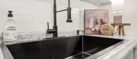 A kitchen sink with a modern faucet, a bottle of hand soap, and a decorative item on the countertop.