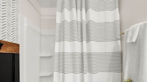 A bathroom with a shower curtain featuring a black and white striped pattern, a white bathtub, a white towel hanging on a rack, and a small potted plant on the edge of the bathtub. - Fort Polk Cozy 2BR Stay l Monthly & Extended Stays (Leesville)