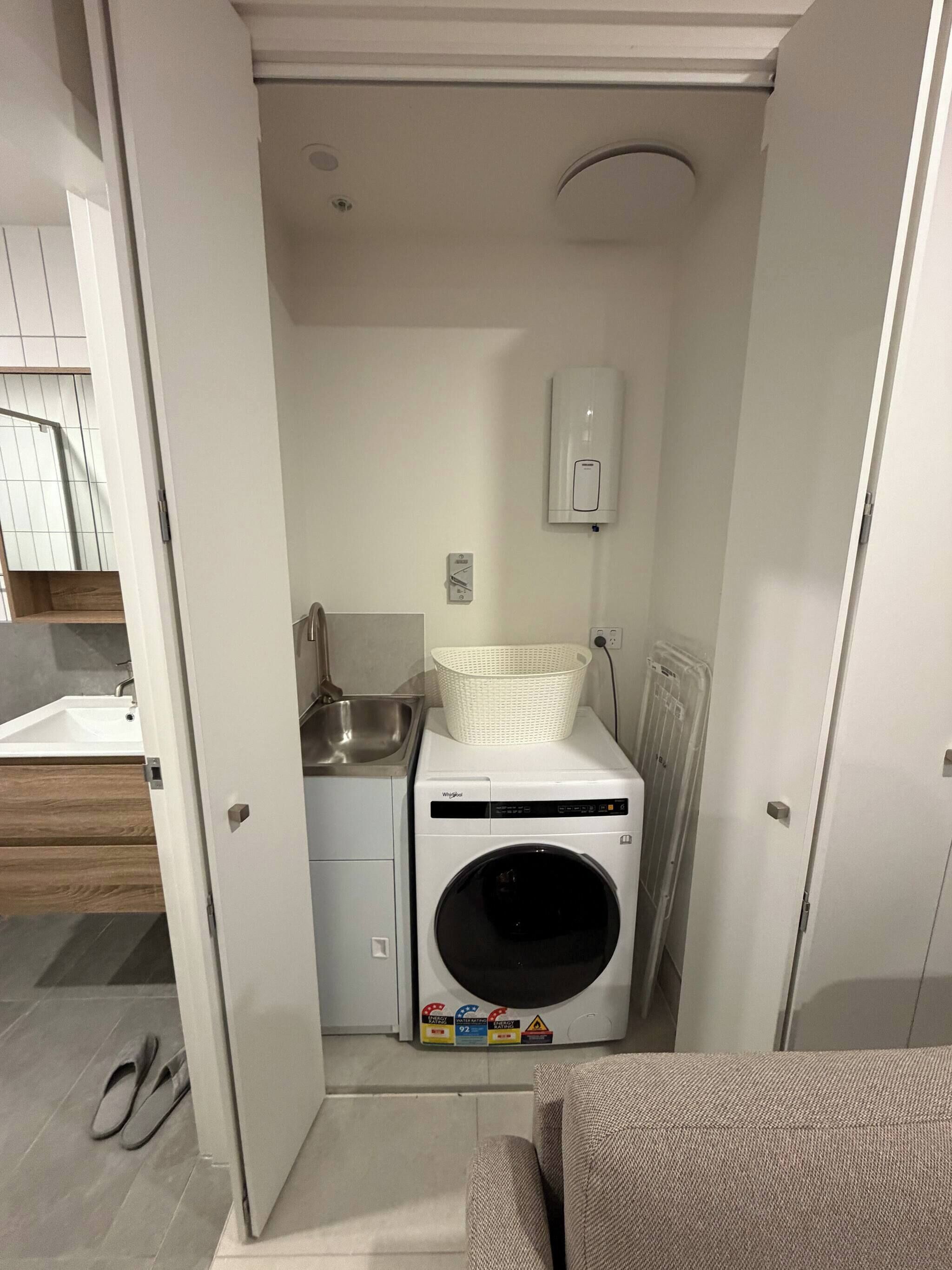 Une petite buanderie comprenant un lave-linge, un évier et un panier blanc posé sur un plan de travail.