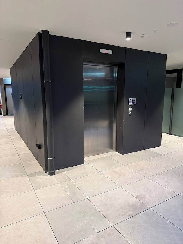 A modern elevator with a digital display, located in a hallway with tiled flooring. - G6 Gungahlin Brand new (Canberra)