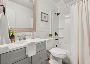 A bathroom with a white sink, a toilet, a shower with a curtain, and a mirror. - Fort Polk Cozy 2BR Stay l Monthly & Extended Stays (Leesville)