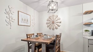Uma área de refeições com mesa de madeira, quatro cadeiras, lustre e decoração de parede.