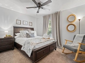 A bedroom with a bed, a nightstand, a chair, a ceiling fan, and two wall-mounted mirrors.