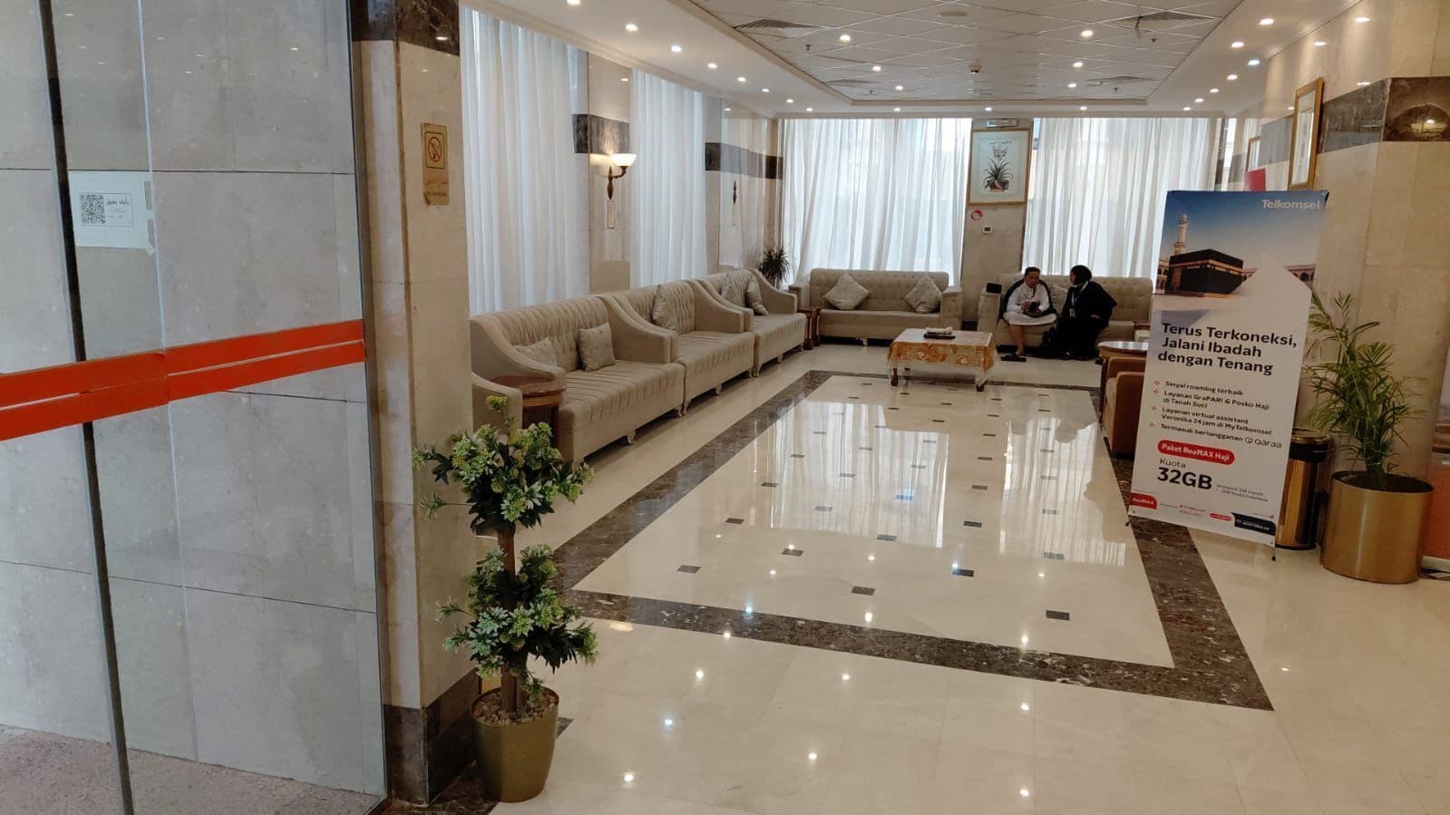Un vestíbulo de hotel con mostrador de recepción, sofás y una planta grande en maceta.
