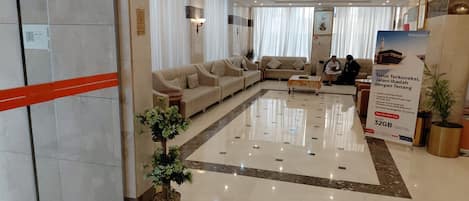 Un vestíbulo de hotel con mostrador de recepción, sofás y una planta grande en maceta.