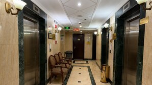 Rebedor d'hotel amb dues ascensors, una taquilla d'informació i una zona d'espera amb cadires.