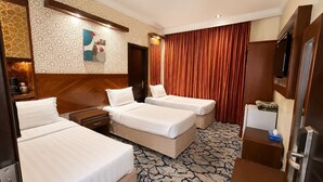 Habitación de hotel con dos camas, cabecero de madera, pared con diseño, cortina roja, televisor de pantalla plana y minibar.